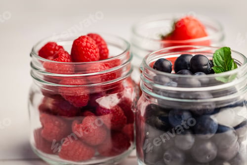 Preview: Glass jars of fresh berries on wooden table