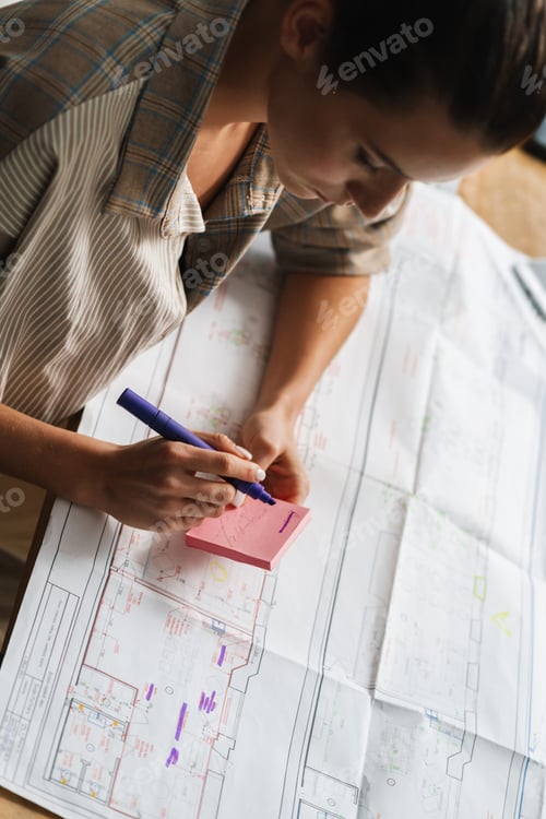 Preview: Young woman drinking coffee Young brunette woman working with drawings while sitting at desk