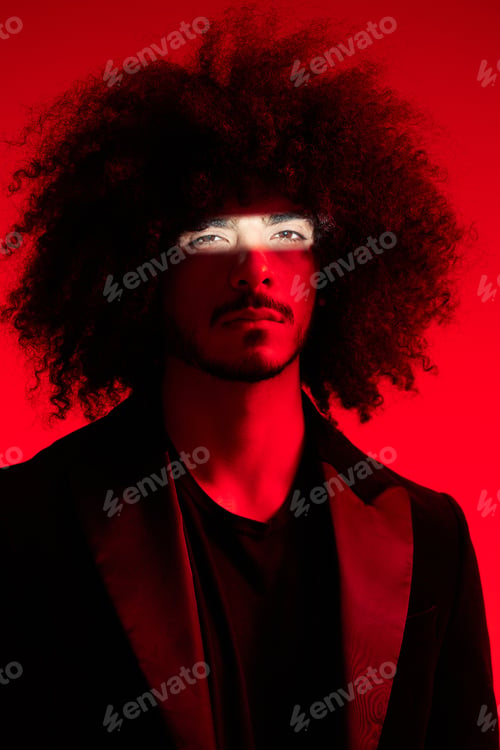 Preview: Fashion portrait of a man with curly hair on a red background, multinational, colored light, trendy