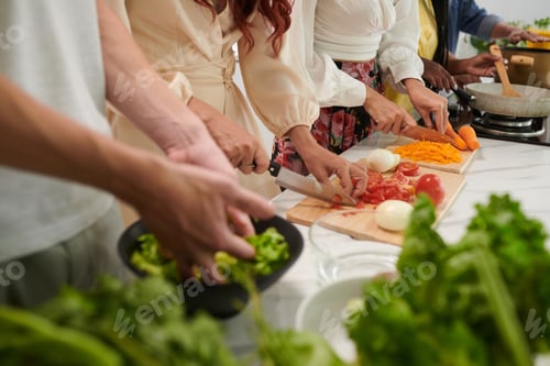 Preview: Row of young intercultural friends with sharp knives chopping fresh vegetables