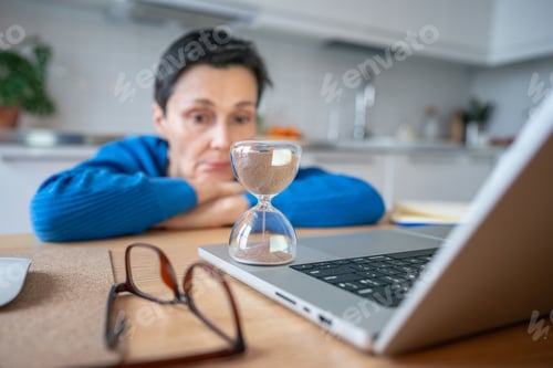 Preview: Time measured by looming deadlines. Upset sad woman with head on arms remote work on laptop, burnout