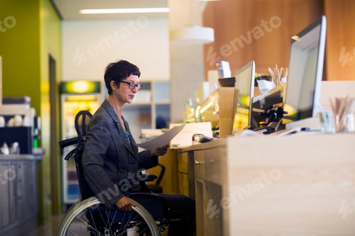 Preview: Woman in wheelchair, sitting at desk, looking at document