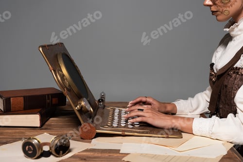 Preview: cropped view of woman typing on steampunk laptop at table isolated on grey