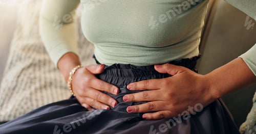 Preview: Hands, menstruation and stomach pain with woman on sofa in living room of home for menstrual cramps