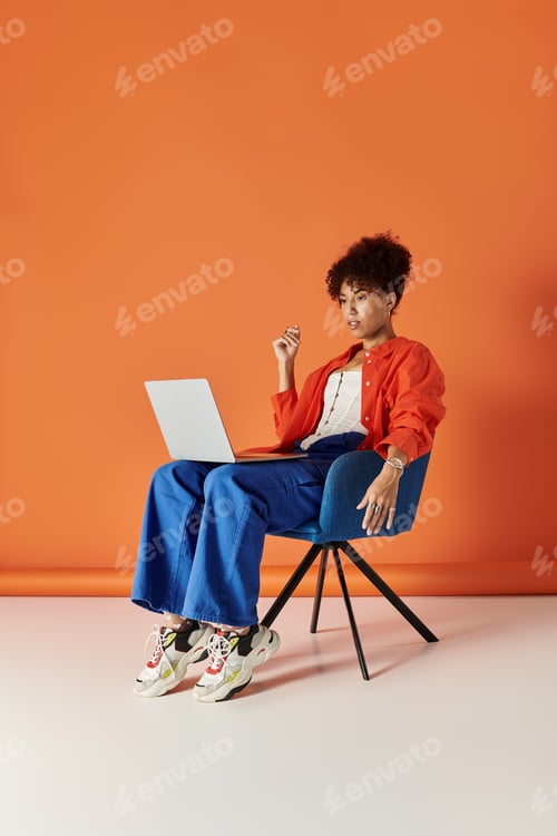 Preview: Curly haired woman in vibrant outfit engages with device in bright studio setting