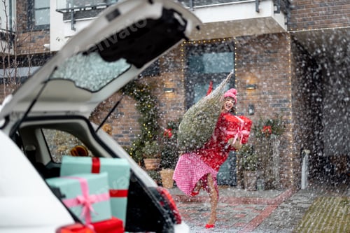 Preview: Woman carries Christmas tree and gift box near a house