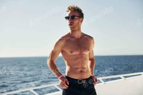 Preview: In sunglasses. Young male tourist is on the yacht on the sea. Conception of vacation