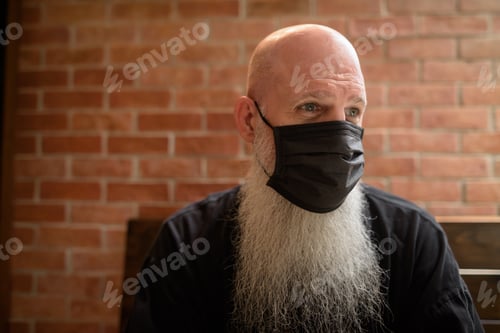 Preview: Mature man with long gray beard wearing face mask to protect from corona virus Covid 19 while