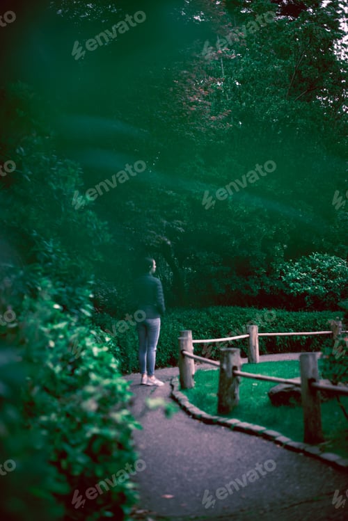 Preview: Vertical shot of a female standing on the walking street by a tree-covered garden