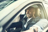 Preview: African businessman smiling while driving his car in the city