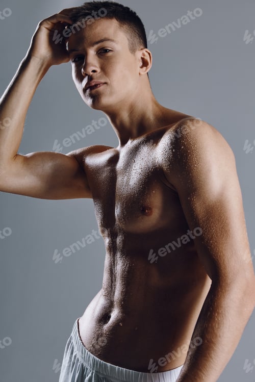 Preview: sports guy in white shorts holds his hand near the face on a gray background and muscles