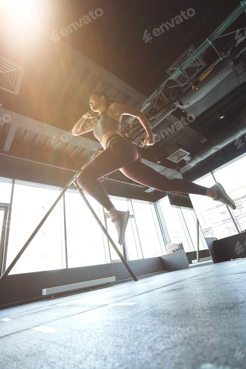 Preview: Bottom view of athletic woman in sportswear jumping or running while working out at industrial gym