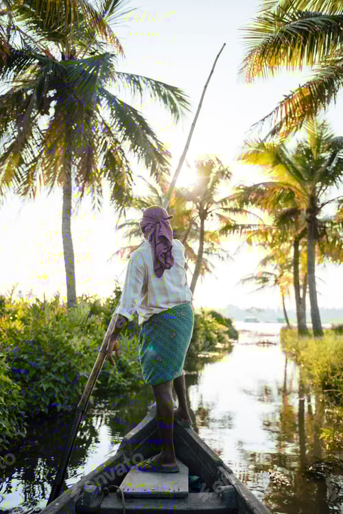 Preview: A person gracefully navigates a boat through a serene waterway lined with palm trees at golden hour.