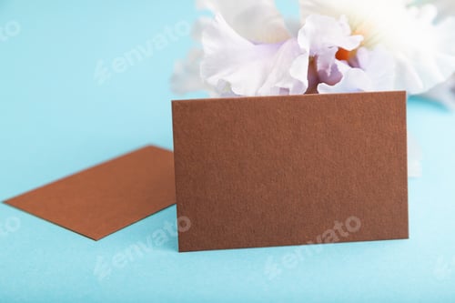 Preview: Brown business card with lilac iris flowers on blue pastel background. side view, copy space.