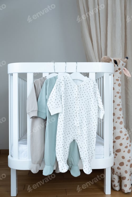 Preview: Baby bodysuit on hanger on bed. Cute children's clothes, baby chair, soft giraffe, retro car