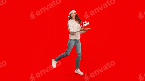 Preview: woman in Santa hat leaps with gift box, red background