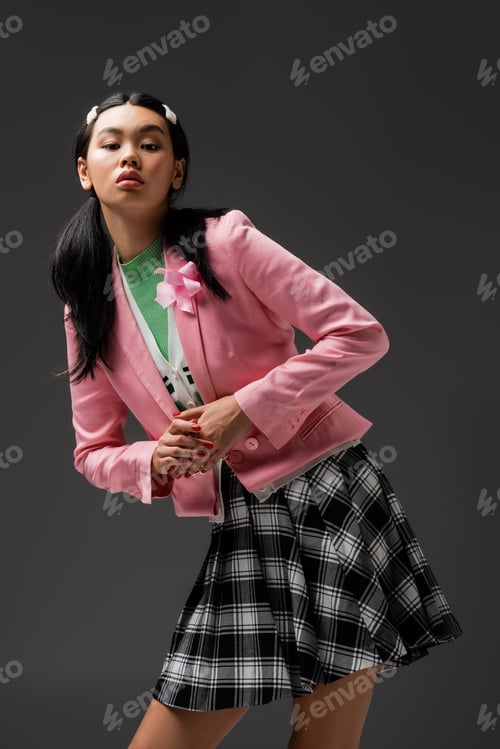 Preview: Pretty asian woman in skirt and pink jacket looking at camera isolated on grey