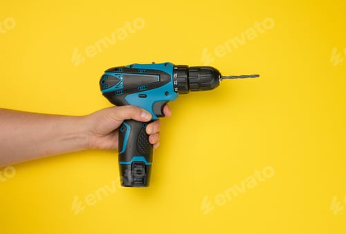 Preview: Female hand holds a cordless drill on a yellow background. Tool for work
