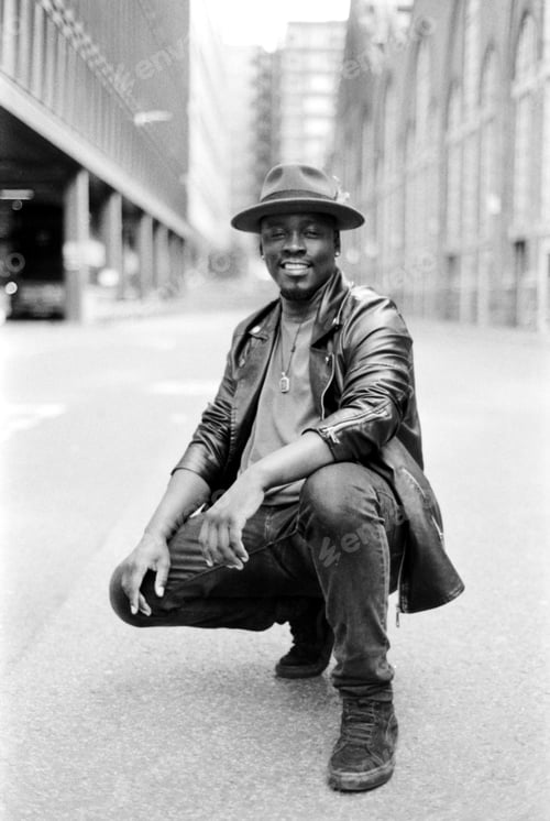 Preview: Smiling male model posing in the street squatting on the asphalt.