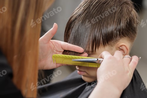 Preview: Hairdresser cutting boy bangs with scissors and comb at barbershop