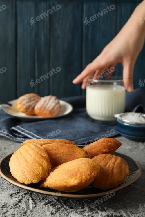 Preview: Madeleine cakes, glass of milk and hand on blue wooden background, close up