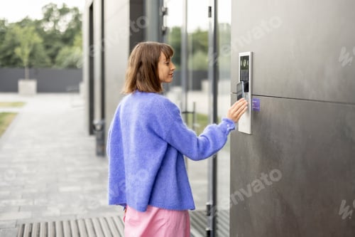 Preview: Young stylish woman getting access to the building by attaching smartphone to intercom
