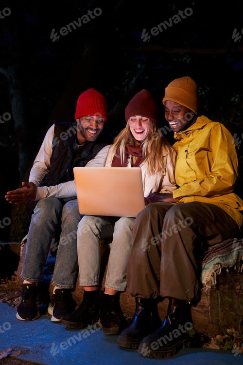 Preview: Three cheerful Mixed race Friends Using computer, sitting together at camping in the forest.