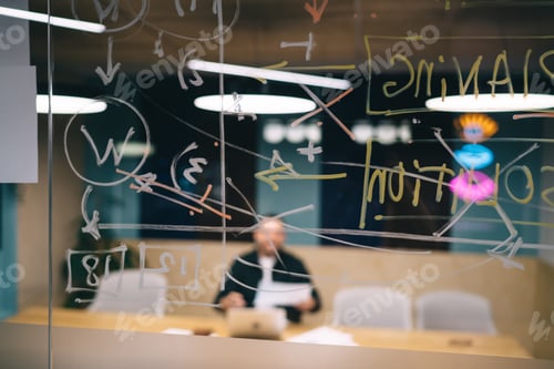 Preview: Working businessman seen through glass wall with formulas and charts