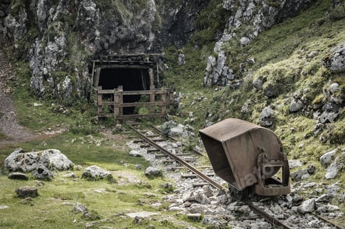 Vista previa: Closeup of an abandoned mine with an old wagon on the tracks surrounded by rocks