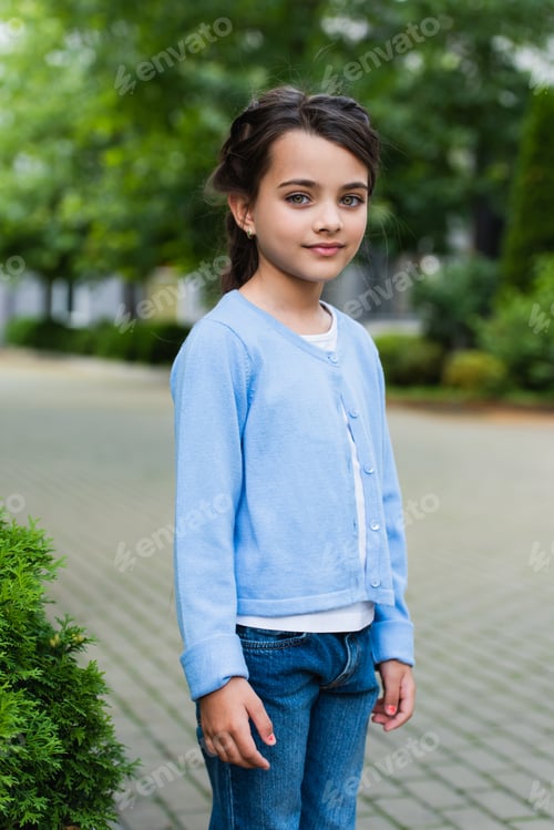 Preview: smiling brunette girl in blue jumper looking at camera on blurred street