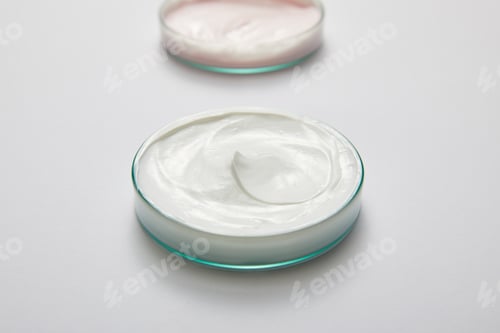 Preview: Selective focus of laboratory glassware with white and pink cosmetic cream on grey background