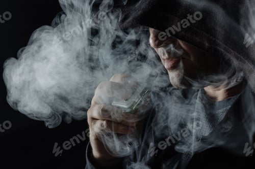 Preview: a man smokes a vape electronic cigarette in black clothes on a dark background, close-up