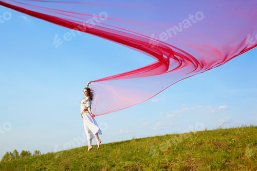 Preview: Outdoor Portrait Of Beautiful Hippie Girl Running With Big Piece Of Red Light Cloth Under The Blue