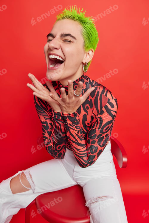 Preview: Glad teenage girl exclaims from joy sits comfortably on chair reacts emotionally on funny thing has