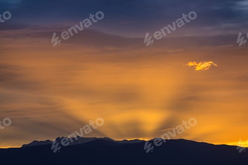 Preview: Sun behind dark mountain silhouettes, with colorful sky and clouds