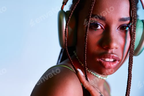 Preview: young african american woman with dreadlocks in wireless headphones looking at camera on blue