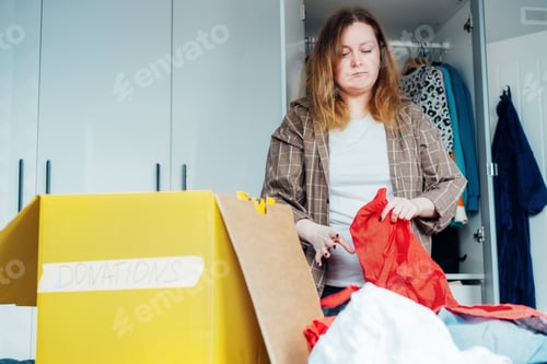 Preview: Woman selecting clothes from her wardrobe for recycling, donating to a Charity shop. Decluttering,