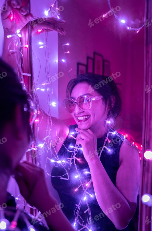 Preview: A young woman is smiling and posing looking at the mirror wearing sunglasses surrounded by lights