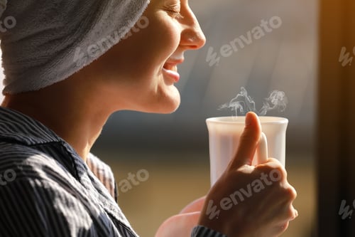 Preview: Beautiful young woman with bath towel on head holds a white cup of hot coffee or tea at home by the