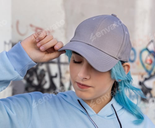 Preview: Blue haired Teenage girl in blue hoodie and baseball cap staying against graffiti wall