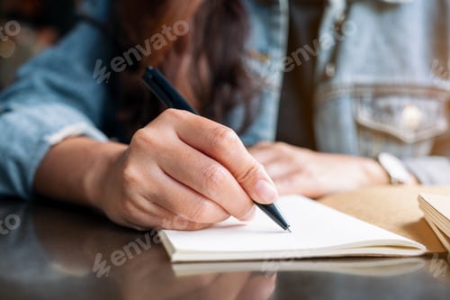Preview: Closeup image of a woman writing on a blank notebook on wooden table