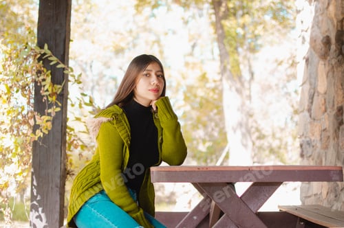 Preview: Caucasian young female sits on a picnic table in the park surrounded by lush trees