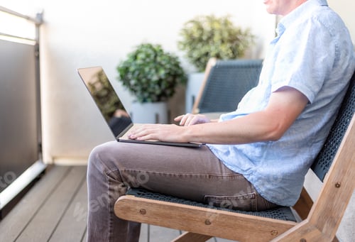 Preview: Young man using laptop while sitting outside on an apartment balcony