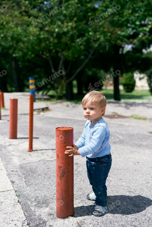 Preview: Kid stands on the street near a little red metal post against a background of trees