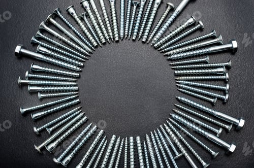 Preview: A lot of wood screws, lying on a black, rough table, flat view from above.