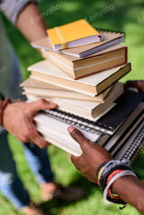 Preview: close-up partial view of students holding pile of books in park