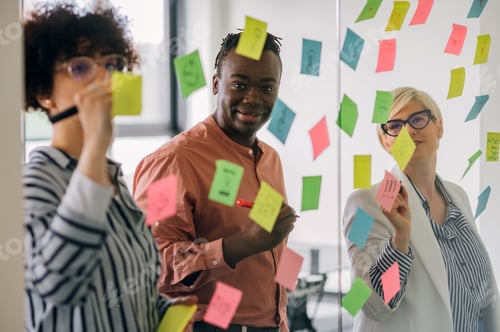 Preview: Multiracial team at work writing ideas on sticky notes on the glass wall