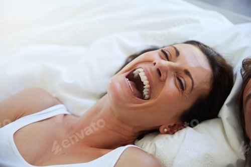 Preview: Shot of a woman laughing while relaxing in bed alongside her husband
