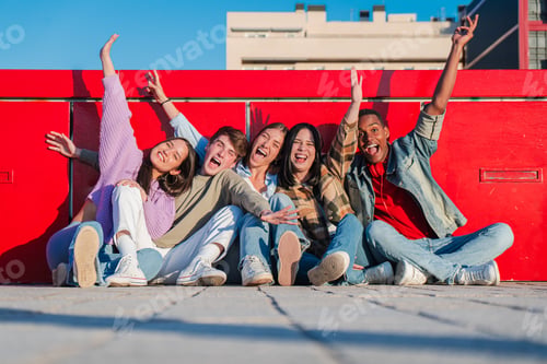Preview: Group of excited teenagers sitting at the floor and spreading their arms over red background. Five