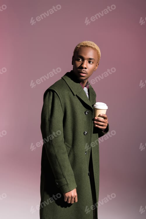 Preview: Stylish young african american man holding paper cup and looking away isolated on violet background